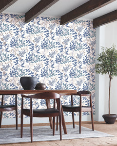 Dining room featuring a wooden table and chairs, decorative bowls on the table, Eden Retreat Wallpaper by York Wallcoverings in a blue and beige floral pattern, exposed ceiling beams, hardwood floor, and a potted tree in the corner.