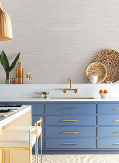 Kitchen scene featuring blue cabinets, a wall-mounted brass faucet, and Grass Roots Wallpaper by York Wallcoverings, a light-colored, finely textured wallpaper with horizontal stripes.