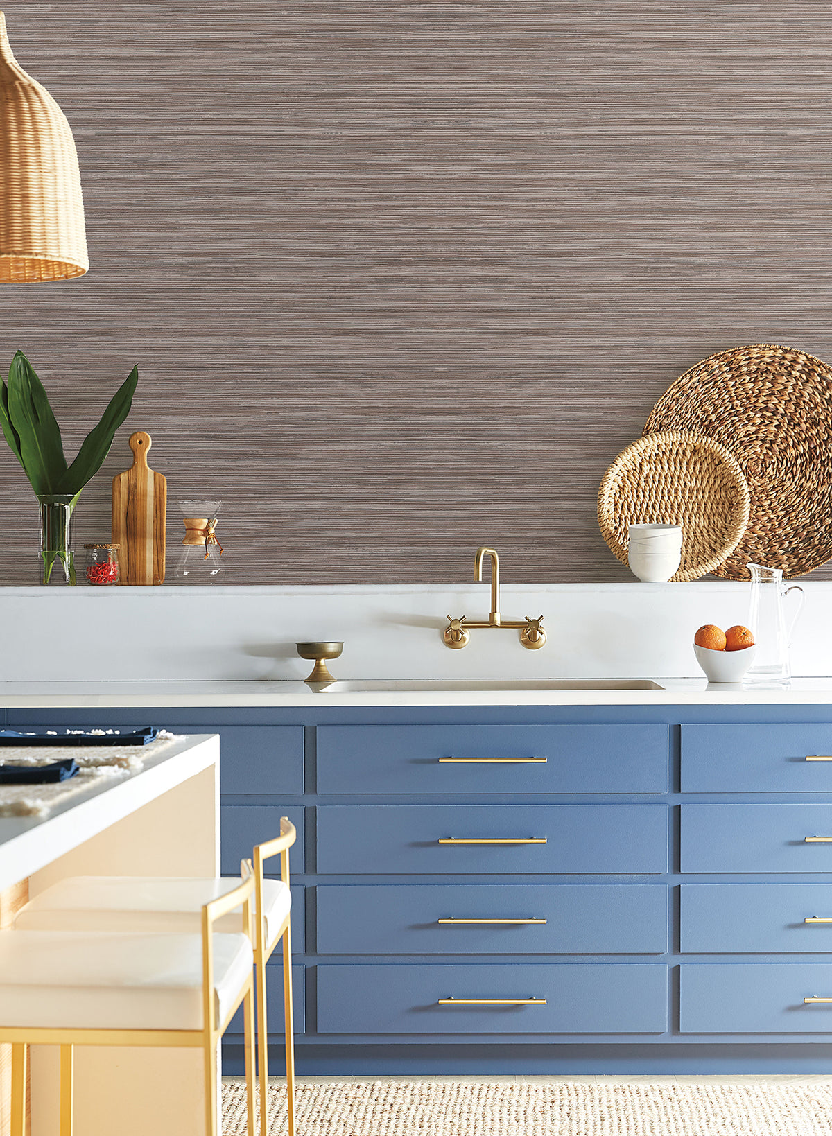 York Wallcoverings Grass Roots Wallpaper with a dark brown horizontal texture above blue cabinets, a gold faucet, and a white countertop.