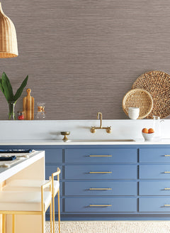 York Wallcoverings Grass Roots Wallpaper with a dark brown horizontal texture above blue cabinets, a gold faucet, and a white countertop.