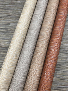 Four rolls of Grass Roots Wallpaper in cream, silver, taupe, and copper displayed diagonally over a dark textured background.