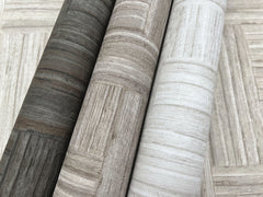 Three rolls of Tesselle Wallpaper featuring a wood-grain geometric pattern in charcoal, taupe, and light gray.