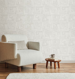 Light-colored Tesselle Wallpaper by York Wallcoverings featuring a repeating geometric pattern of textured squares, shown behind an armchair and a small side table.