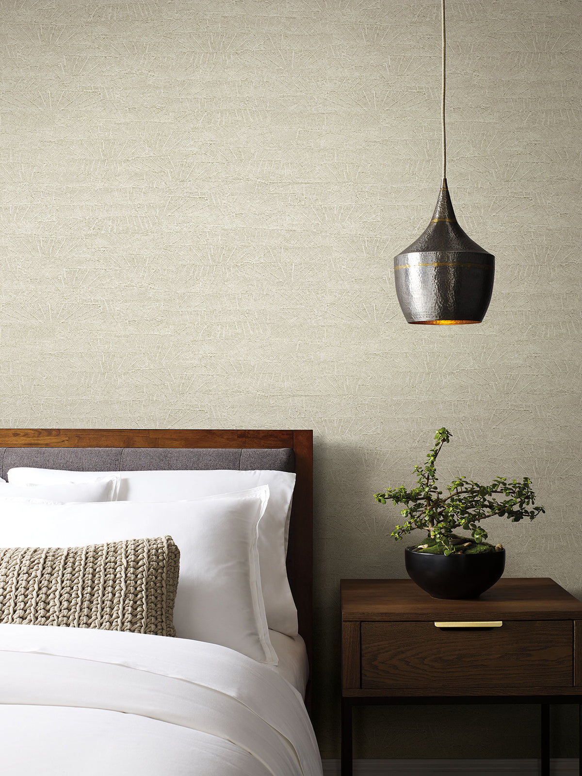 On Deck Wallpaper in beige with a subtle, geometric pattern of thin, intersecting lines, shown on the wall behind a bed and nightstand.