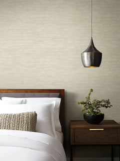 On Deck Wallpaper in beige with a subtle, geometric pattern of thin, intersecting lines, shown on the wall behind a bed and nightstand.