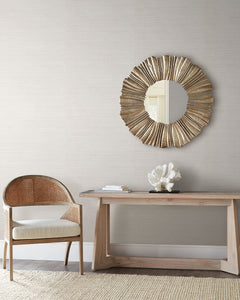 Light gray Tasar Silk Wallpaper by York Wallcoverings behind a console table with a coral sculpture and a round sunburst mirror.
