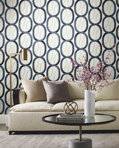 Candice Olson Interlock Wallpaper featuring a repeating pattern of interlocking dark blue and gold-outlined oval rings on a white background, behind a sofa and coffee table.