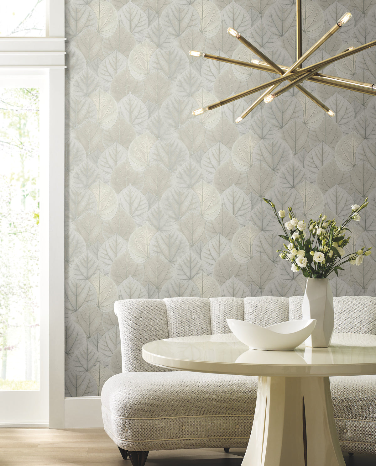Candice Olson Leaf Concerto Wallpaper featuring a repeating pattern of overlapping, light-colored leaves on a wall behind a curved sofa and dining table.
