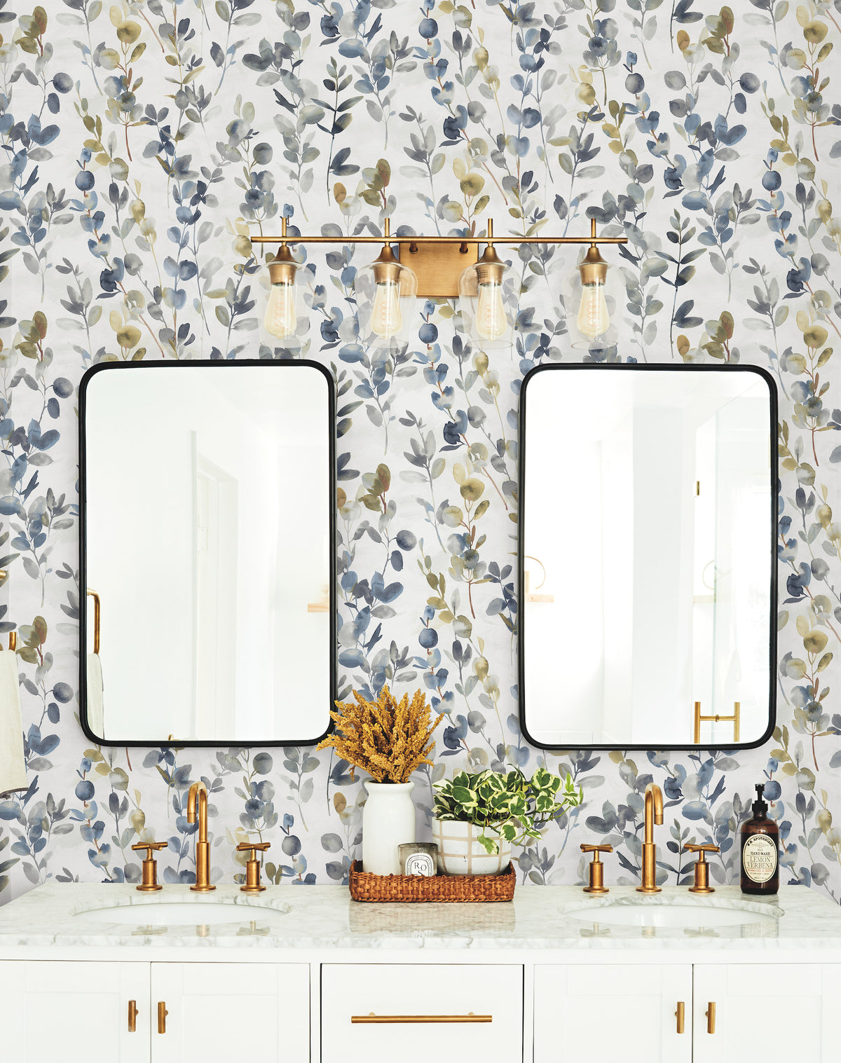 Bathroom vanity with two mirrors and gold faucets set against a wall covered in Candice Olson Joyful Eucalyptus Wallpaper.