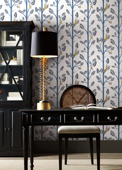 Blue Aviary Branch peel and stick wallpaper in a home office with a dark desk and lamp.