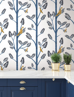 Aviary Branch blue peel and stick wallpaper above a white marble countertop and blue kitchen cabinets.