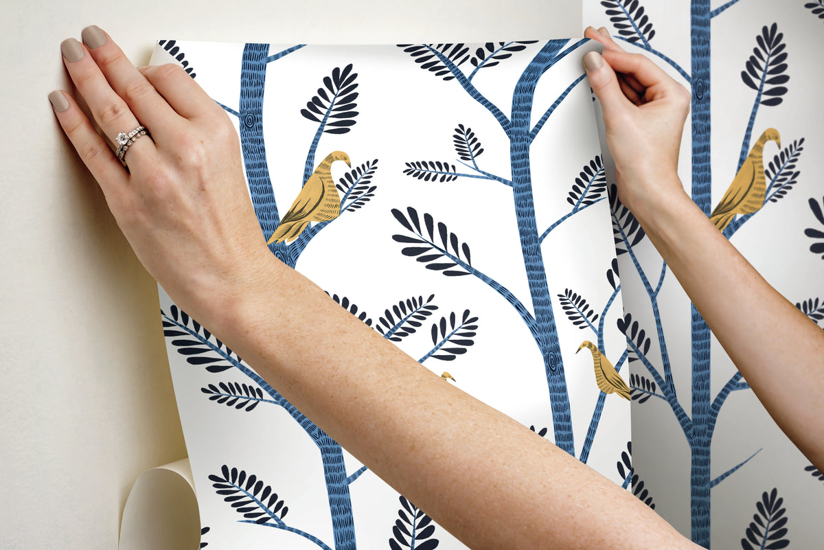 Hands applying blue Aviary Branch peel and stick wallpaper with birds to a wall.