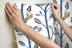 Hands applying blue Aviary Branch peel and stick wallpaper with birds to a wall.