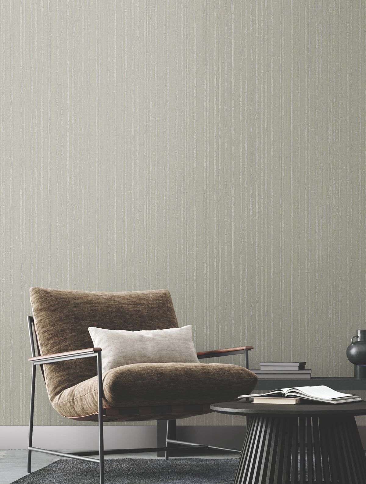 A brown lounge chair and small round side table sit in front of a wall covered in Ronald Redding Vintage Tin Wallpaper by York Wallcoverings, featuring a light gray pinstripe pattern.