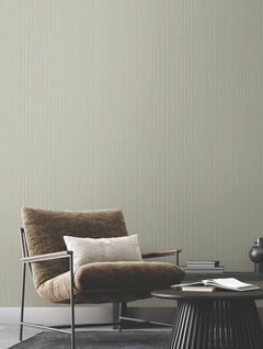 A brown lounge chair and small round side table sit in front of a wall covered in Ronald Redding Vintage Tin Wallpaper by York Wallcoverings, featuring a light gray pinstripe pattern.
