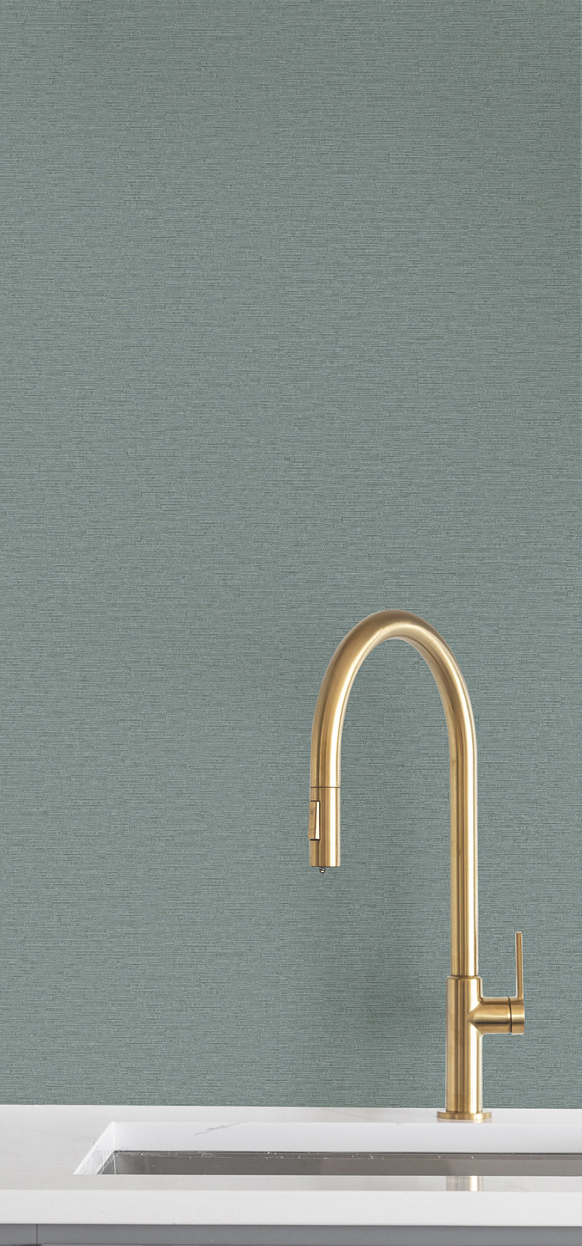 Ronald Redding Cantilever Wallpaper in teal with a fine, horizontal texture installed behind a brass kitchen faucet and white countertop.