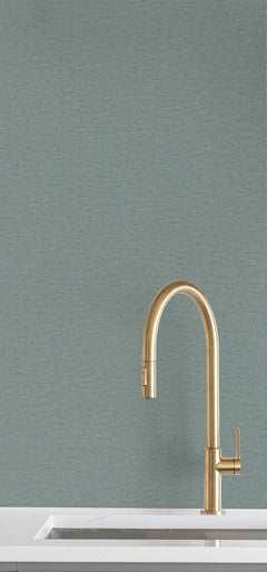 Ronald Redding Cantilever Wallpaper in teal with a fine, horizontal texture installed behind a brass kitchen faucet and white countertop.