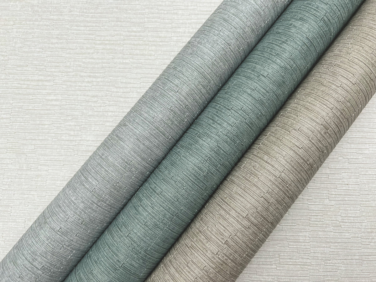Three diagonal rolls of Ronald Redding Cantilever Wallpaper featuring a textured, linear pattern in shades of grey, muted teal, and bronze, set against a light grey background of the same pattern.