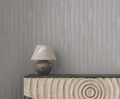 Gray Ronald Redding Newel Wallpaper with a vertical striped pattern behind a table lamp and a carved wooden cabinet.