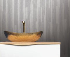 A gold textured vessel sink with a tall gold faucet sits on a white countertop against a wall adorned with Ronald Redding Newel Wallpaper by York Wallcoverings.