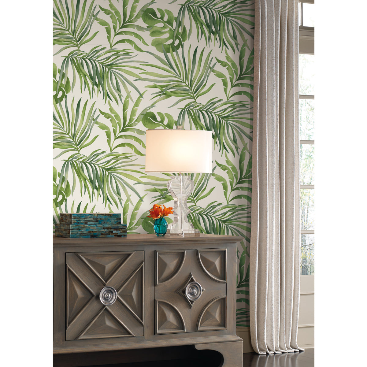 Paradise Palm Wallpaper featuring a pattern of green palm leaves on a cream background, installed behind a wooden cabinet with a table lamp.