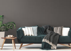 A dark green velvet sofa with patterned and plain cushions, a gray throw, a wooden coffee table with candles, and a potted plant sit against a Cascade Glimmer Wallpaper by York Wallcoverings in a modern living room.
