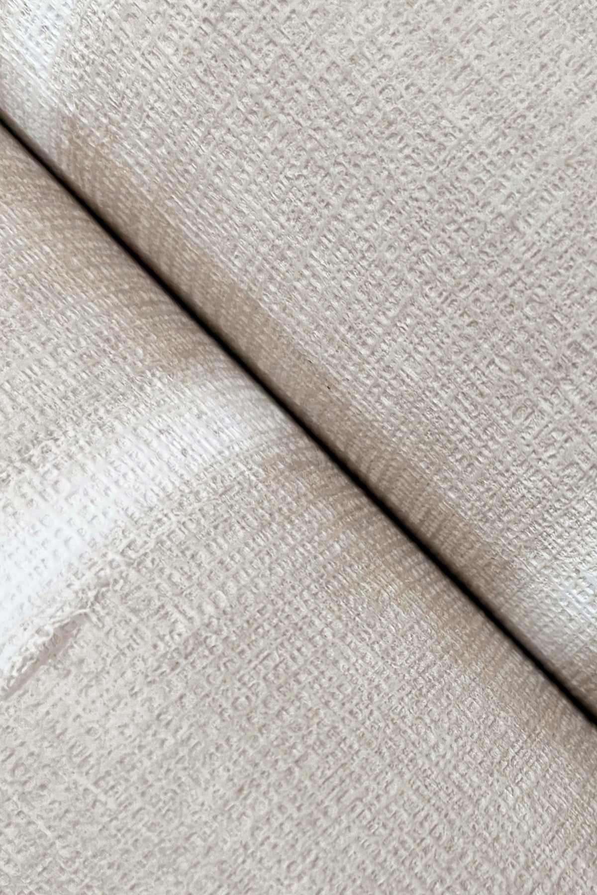 Close-up view of two rolls of York Wallcoverings’ Resound Wallpaper placed side by side, highlighting the subtle woven pattern in textured beige and a visible seam where the rolls meet.