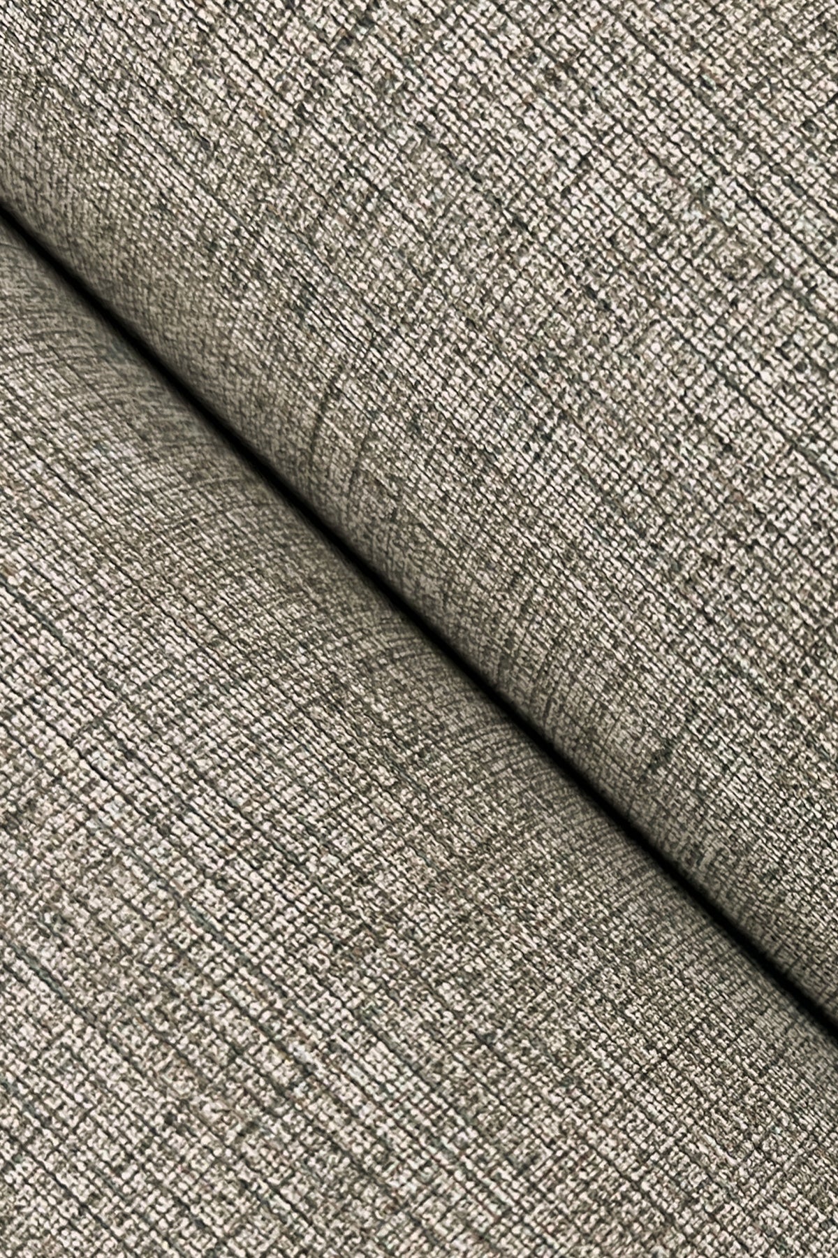 Close-up of Hardy Linen Wallpaper by York Wallcoverings, showcasing its textured, beige surface with a woven, grid-like pattern. The wallpaper is folded diagonally, creating a visible crease and shadow across the image.