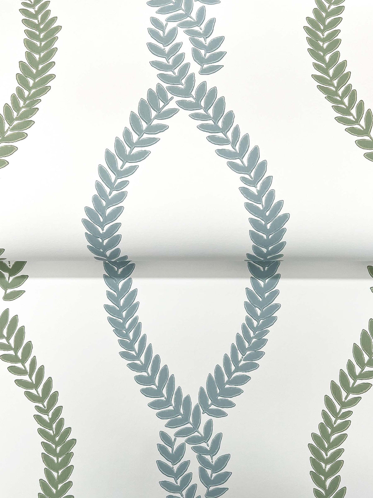 York Wallcoverings’ Laureate Vine Trellis Wallpaper features a repeating pattern of green and blue leafy vines forming oval and curved shapes on a white background.