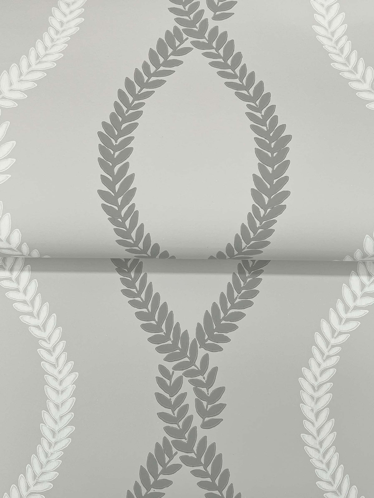 Laureate Vine Trellis Wallpaper by York Wallcoverings features a smooth gray background adorned with a repeating pattern of overlapping laurel wreaths in shades of gray and white, creating a diamond-like design.