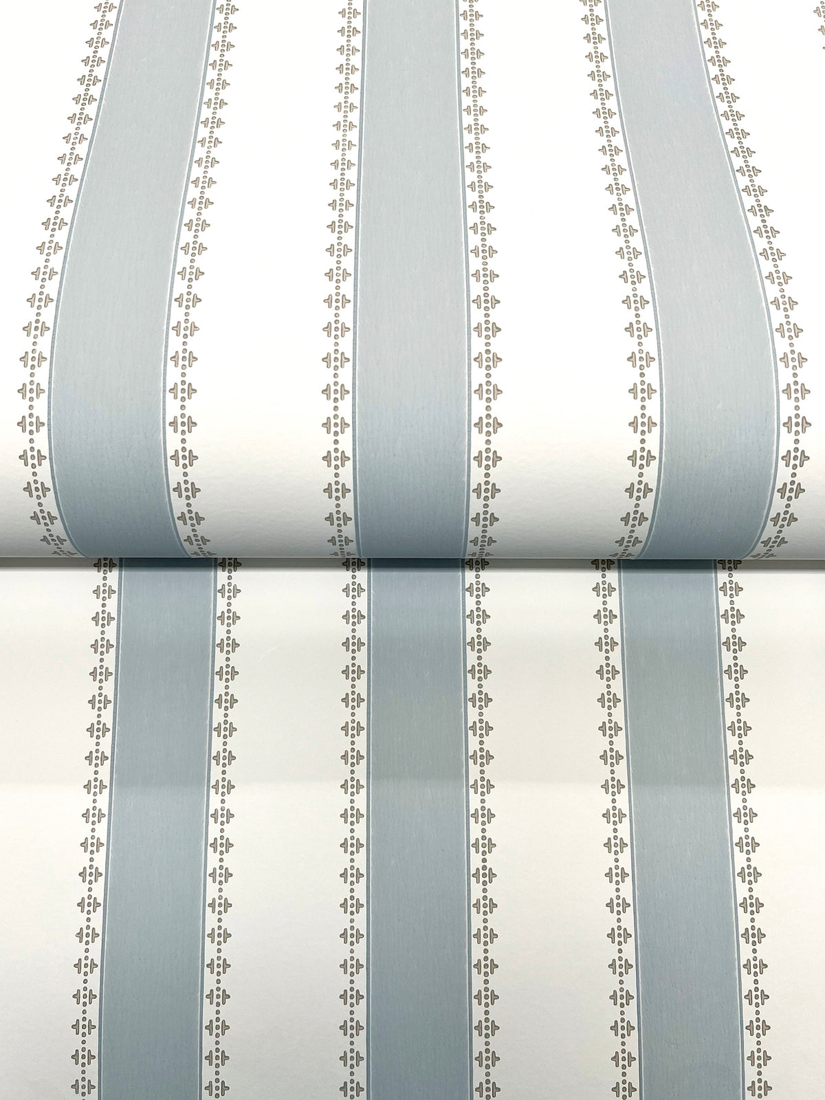 Tilford Awning Stripe Wallpaper by York Wallcoverings features vertical stripes in pale blue and white, accented by thin lines with a small repeating motif for a simple, classic look.