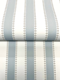 Tilford Awning Stripe Wallpaper by York Wallcoverings features alternating wide light blue and white vertical stripes, separated by narrow beige lines adorned with small leaf patterns. The photo displays a section of the wallpaper rolled out.