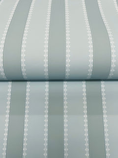The Tilford Awning Stripe Wallpaper by York Wallcoverings features pale blue vertical stripes in varying widths, separated by thin white lines adorned with a small repeating leaf pattern. The wallpaper is shown rolled out on a flat surface.