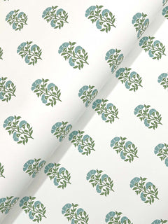 Sylvie Floral Wallpaper by York Wallcoverings features white paper adorned with a repeating pattern of small blue flowers and green leaves, arranged in diagonal rows. The image highlights the wallpaper slightly curled to emphasize its charming floral design.