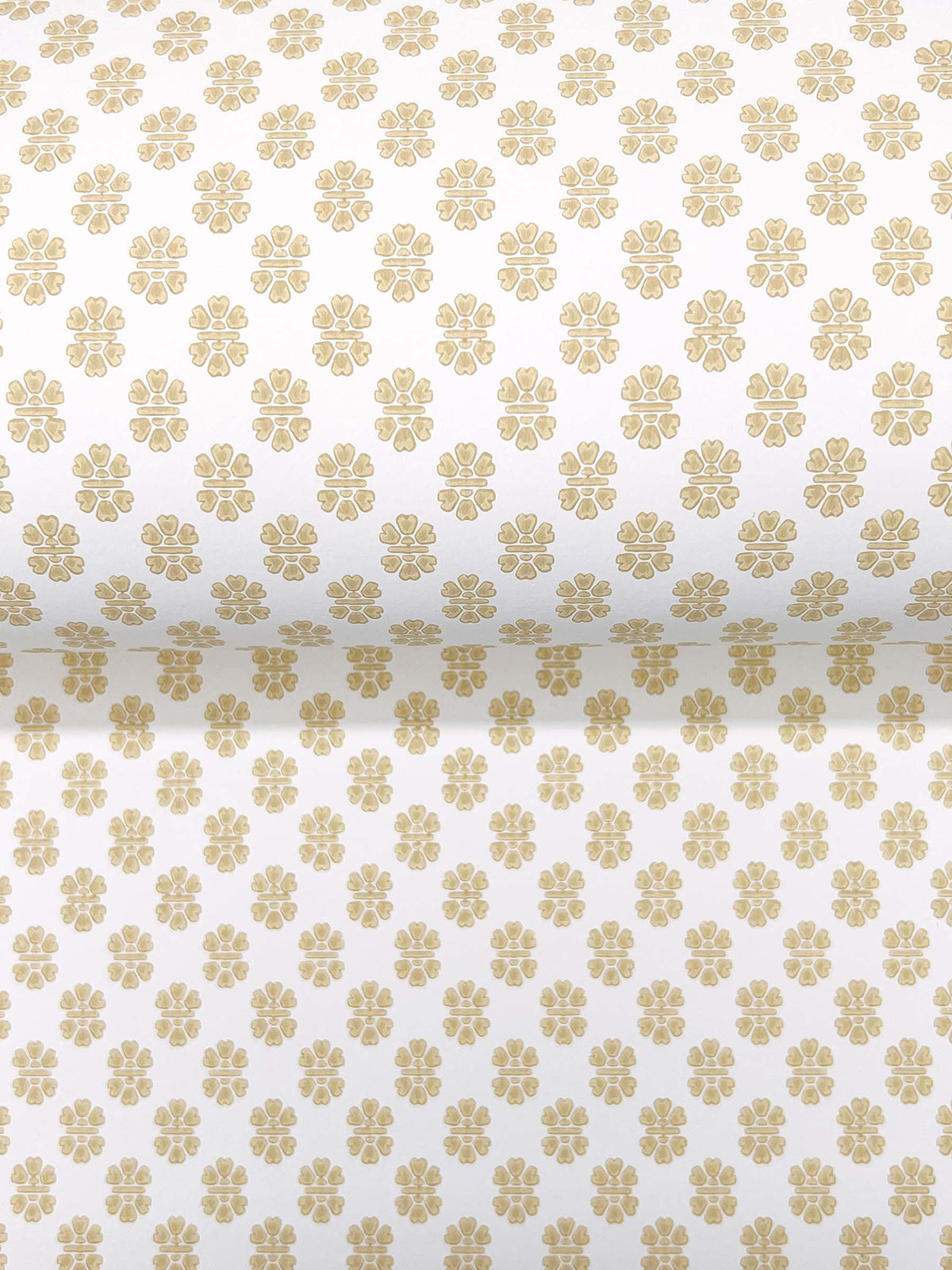 A close-up of Brioni Floral Stamp Wallpaper by York Wallcoverings, featuring a rolled view that reveals both the front and inner sides. The wallpaper displays a beige floral pattern with rows of small, evenly spaced flowers on a white background.