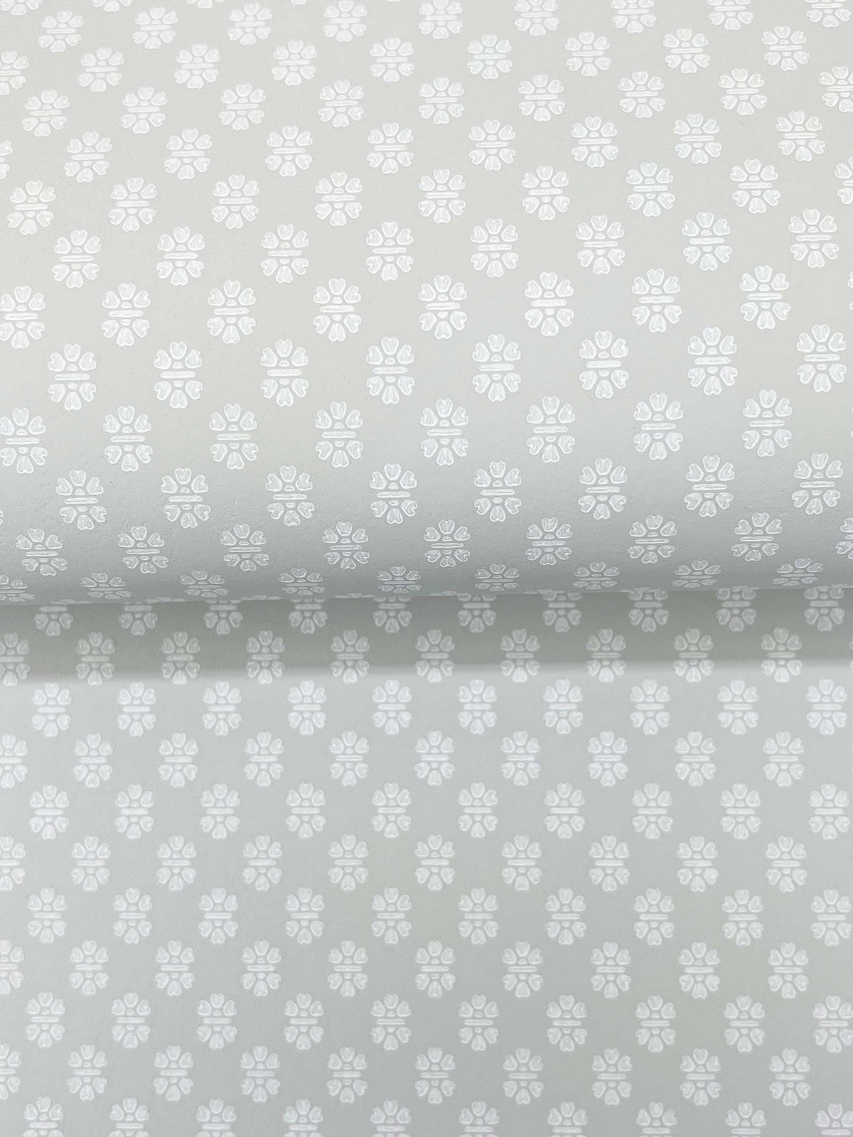 The Brioni Floral Stamp Wallpaper by York Wallcoverings features a light grey backdrop adorned with a subtle, repeating pattern of small white four-petaled flowers, creating a soft, delicate, and uniform appearance across the surface.