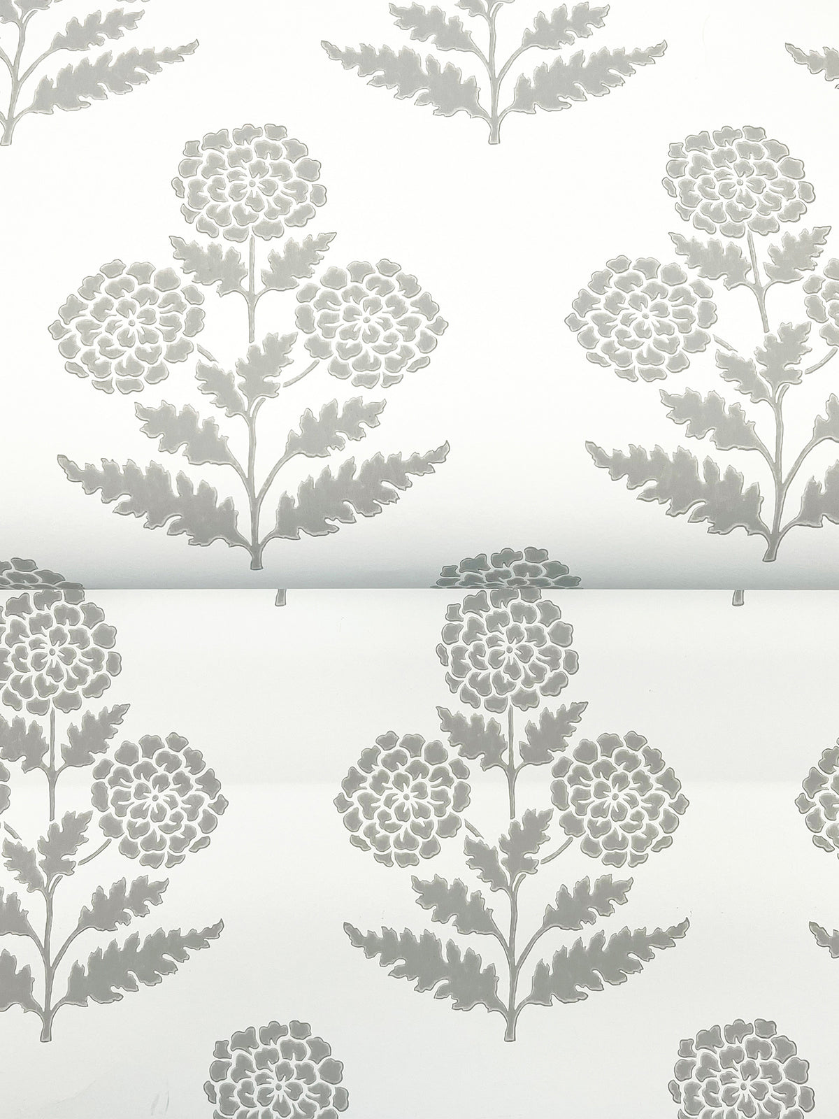 The Souci Marigolds Wallpaper by York Wallcoverings features a repeating gray floral pattern with stylized flowers and leaves printed on a white background, displayed here on a slightly curled sheet.