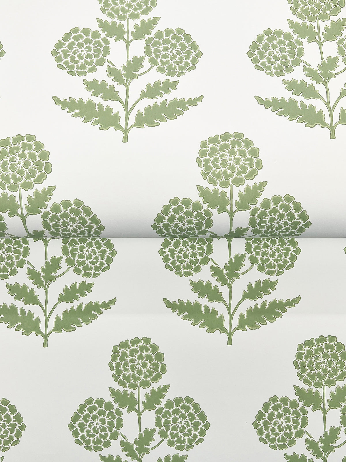 Souci Marigolds Wallpaper by York Wallcoverings features a green floral pattern with stylized marigold flowers, each displaying round clusters of petals and leafy stems, all arranged in a repeating, symmetrical design on a white background. The wallpaper is shown partially rolled out.