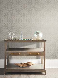 A wooden bar cart with glasses, a bottle, a tray, and a decorative globe sits against a wall adorned with Serendipity Wallpaper by York Wallcoverings. A piece of driftwood rests on the lower shelf.
