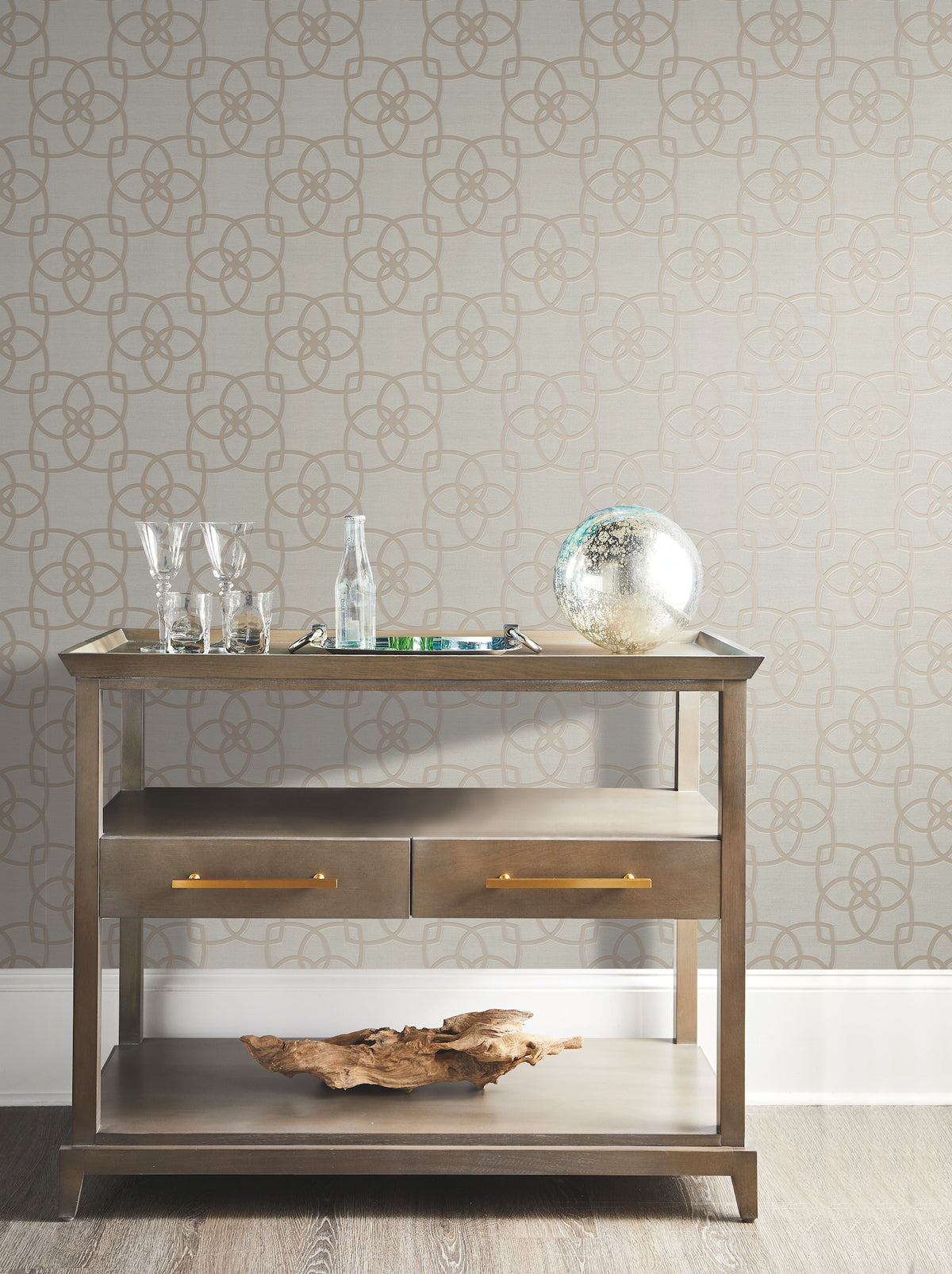 A wooden bar cart with glassware, a bottle, a decorative globe, and a driftwood piece sits against a York Wallcoverings Serendipity Wallpapered wall on a hardwood floor.