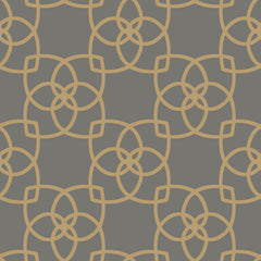 The Serendipity Wallpaper by York Wallcoverings features a symmetrical, seamless pattern of interlocking gold geometric shapes forming a floral motif on a dark gray background, creating a modern and decorative look.
